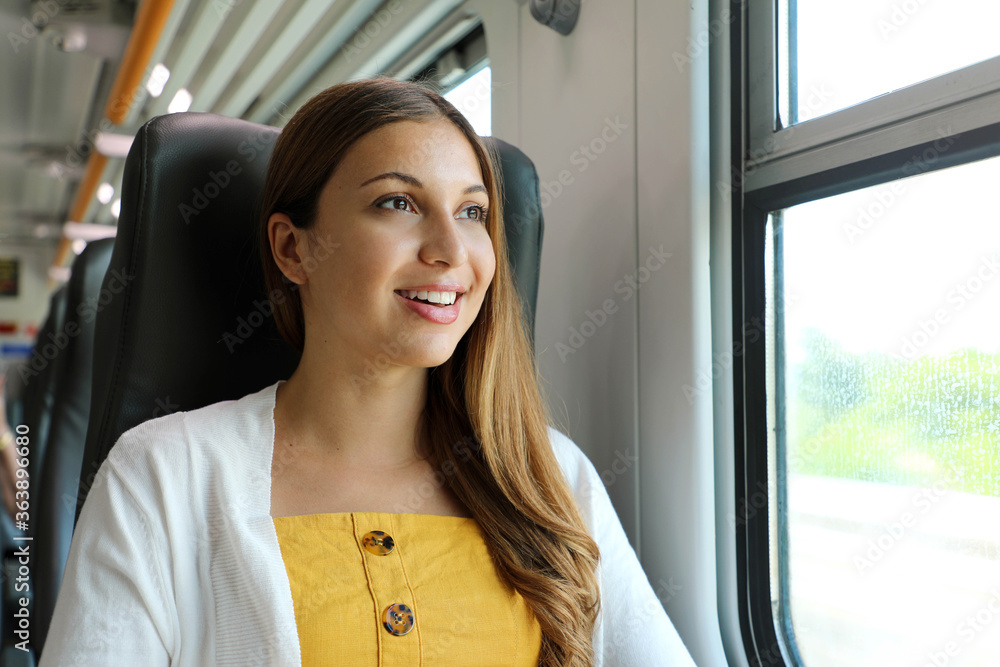 Portrait of young woman looking through the train window. Happy train passenger traveling sitting in a seat and looking through the window. Portrait of young woman looking through the train window. Happy train passenger traveling sitting in a seat and looking through the window.