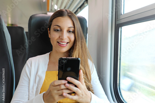 Smiling business woman using smartphone social media app while commuting to work in train. Young woman sitting in transport enjoying travel.