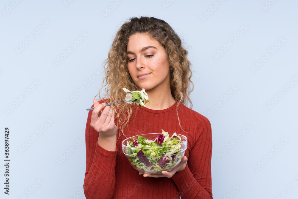 Young blonde woman with curly hair holding a salad over isolated wall Young blonde woman with curly hair holding a salad over isolated wall