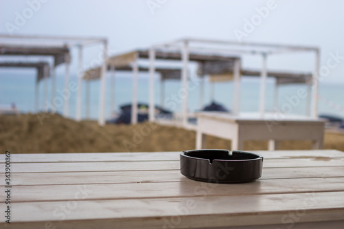 Focus on the ashtray on the beach bar table. It   s a bad season and there are no people.