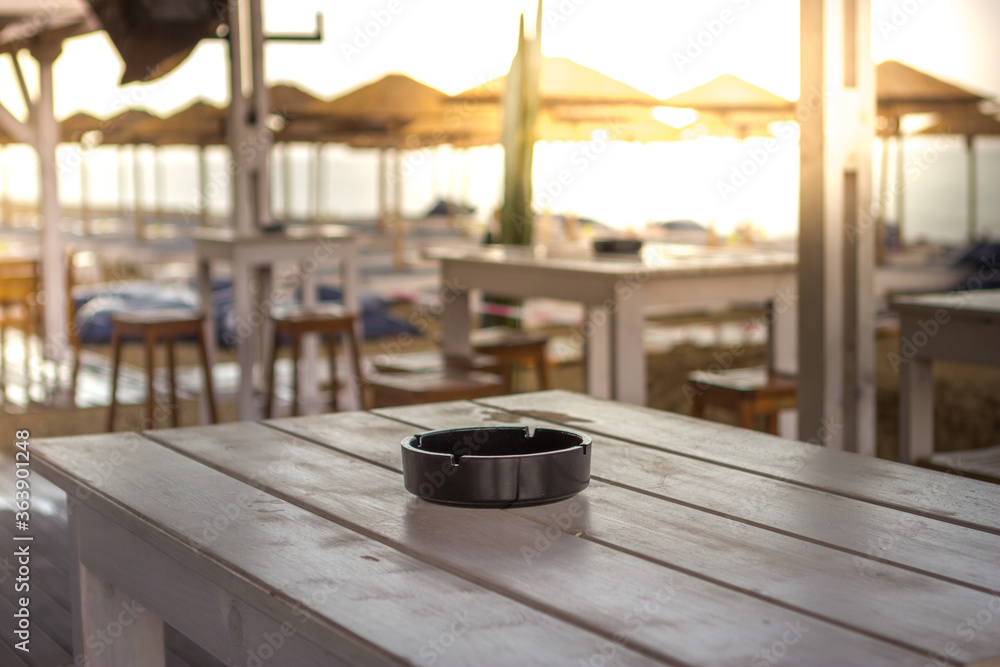 Focus on the ashtray on the beach bar table. It is a bad season and there are no people, although it is a beautiful and sunny day. Focus on the ashtray on the beach bar table. It is a bad season and there are no people, although it is a beautiful and sunny day.