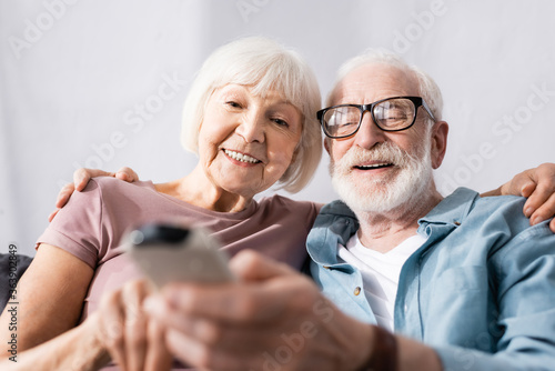 Selective focus of elderly couple smiling and holding remote controller of air conditioner at home