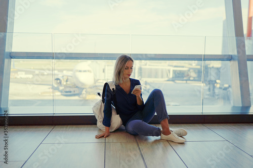 Travel and technology. Pretty young woman using smartphone waiting for boarding in airport terminal.