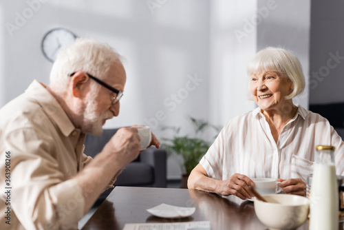 Selective focus of smiling senior woman looking at husband drinking coffee at home