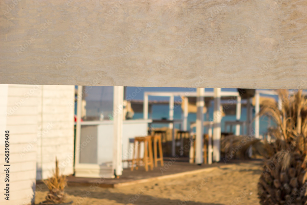 Focus on the wooden board that says beach bar. Behind are umbrellas and sunbeds and blue sea and blue sky. Copy space. Focus on the wooden board that says beach bar. Behind are umbrellas and sunbeds and blue sea and blue sky. Copy space.