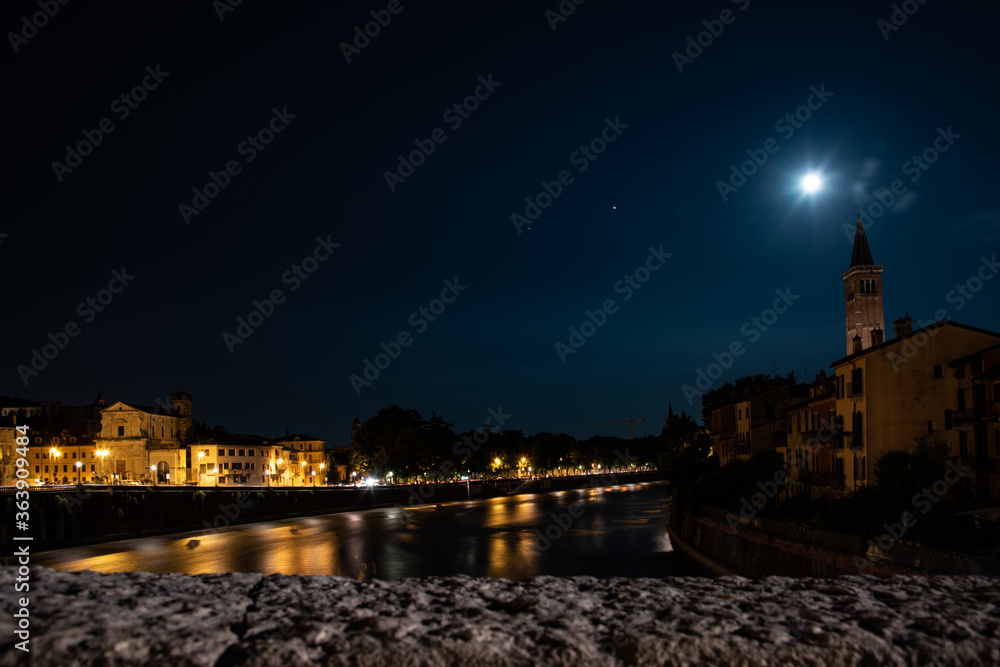 Night photo with moon and star Venus along Adige river with view of the church of Santa Anastasia, city of Verona, Italy.