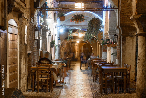 Night photo along via sottoriva with tables of bars, city of Verona, Italy.