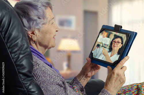 Elderly woman carefully looks at the telemedicine ophthalmologist on the screen of her tablet. She enjoys a remote appointment with the doctor.