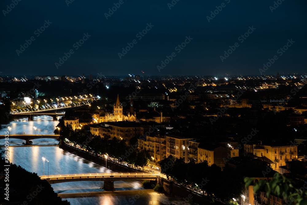 Night photo with moon in sky view along Adige river with view of Ponte Nuovo and Ponte Navi with church of saint Fermo Maggiore, city of Verona, Italy.