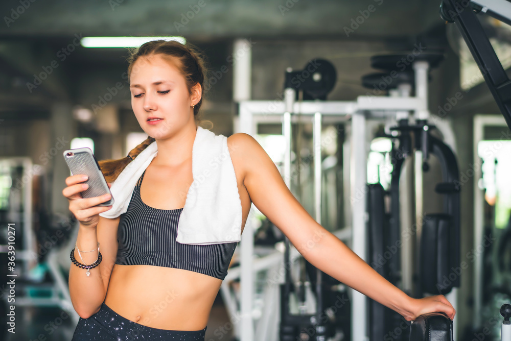 young attractive Caucasian woman using smart phone or cellphone while drinking water and relaxation after hard workout at gym young attractive Caucasian woman using smart phone or cellphone while drinking water and relaxation after hard workout at gym