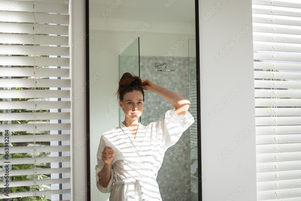 Woman tying her hair while looking in the mirror Woman tying her hair while looking in the mirror