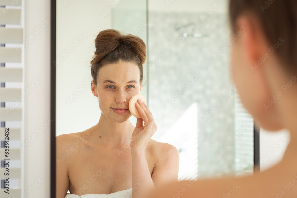 Woman applying makeup to her face while looking in the mirror Woman applying makeup to her face while looking in the mirror
