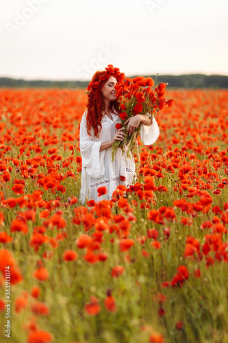 Beautiful redhead smiling woman in wreath with bouquet of poppies on green field © onphotoua