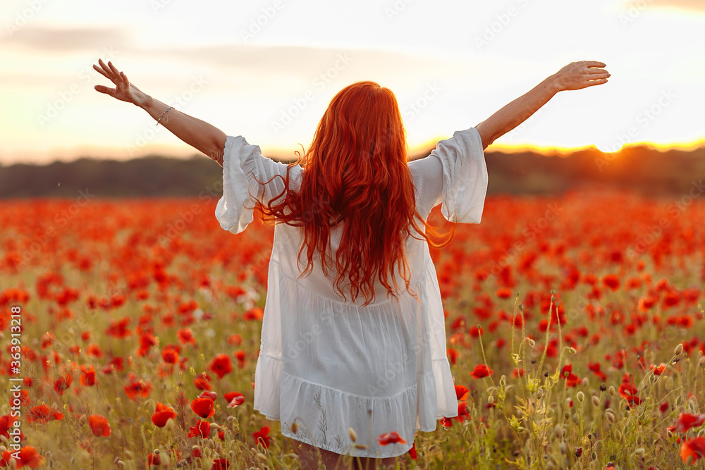 Happy redhead woman in white dress on field of poppies at summer sunset Happy redhead woman in white dress on field of poppies at summer sunset
