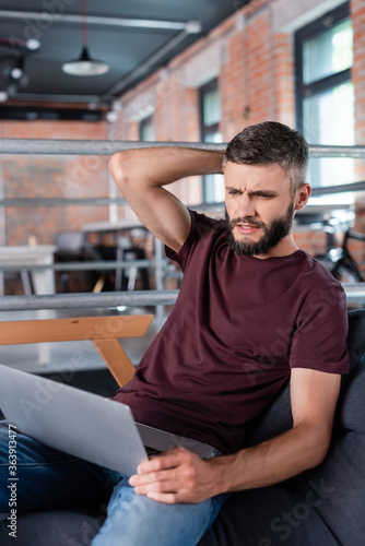 displeased businessman sitting on sofa and using laptop in office