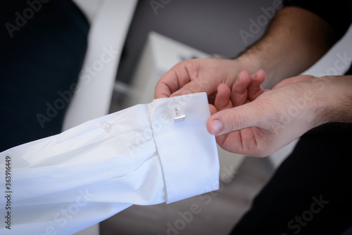 Mani maschili che inseriscono i gemelli nelle asole del polsino della camicia bianca
