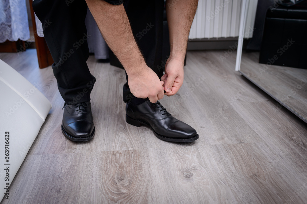 Mani dello sposo che allacciano i lacci della scarpa elegante  nera calzata 
