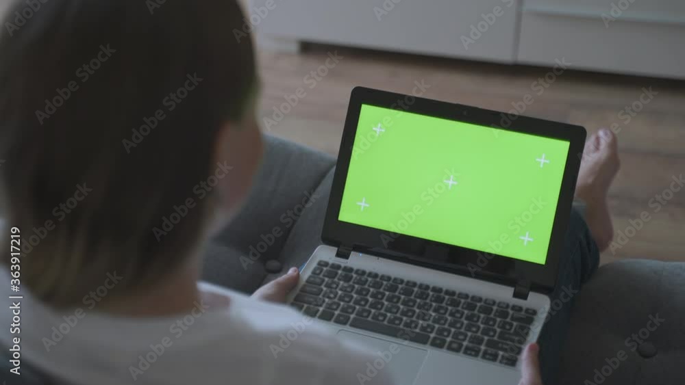 Woman at home sitting on a couch corks on a laptop computer with green mock-up screen. girl using computer, browsing through internet, watching content Woman at home sitting on a couch corks on a laptop computer with green mock-up screen. girl using computer, browsing through internet, watching content