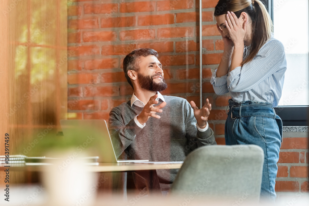 Fototapeta premium selective focus of happy businesswoman covering face near cheerful coworker in office