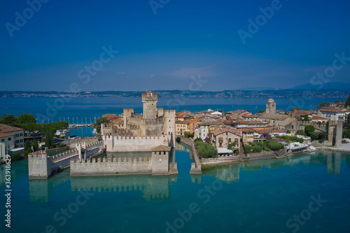 Sirmione, Lake Garda, Italy. The famous Sirmione Castle. Frontal aerial view. Reflections of the castle in the water in the background blue sky