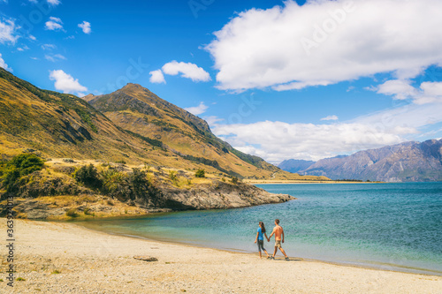 New Zealand travel people tourists visiting Otago region walking on shore of lake Hawea nature landscape. Man and woman happy at beach Near Wanaka. Young tramping hikers adventure lifestyle.