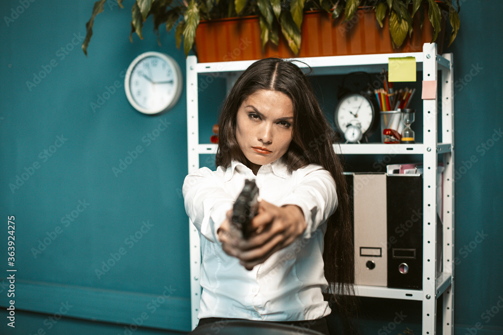 Dangerous woman with gun in office. Crazy or mad angry young businesswoman aiming straight at the camera. Crisis concept. Tinted image. Dangerous woman with gun in office. Crazy or mad angry young businesswoman aiming straight at the camera. Crisis concept. Tinted image.