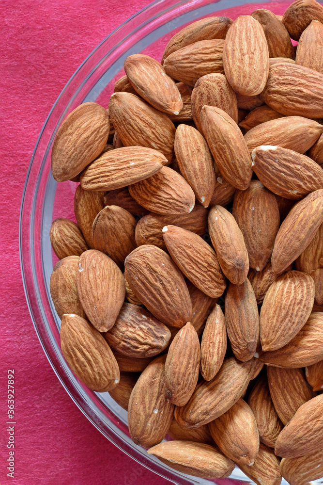 Fototapeta premium Fragment of a glass plate with almond kernels on a red tablecloth