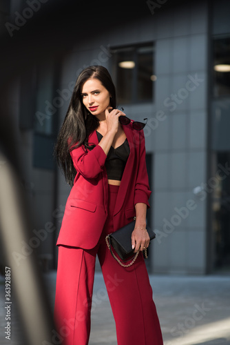 Bussines lady in red suit stands near office. Soft selective focus.