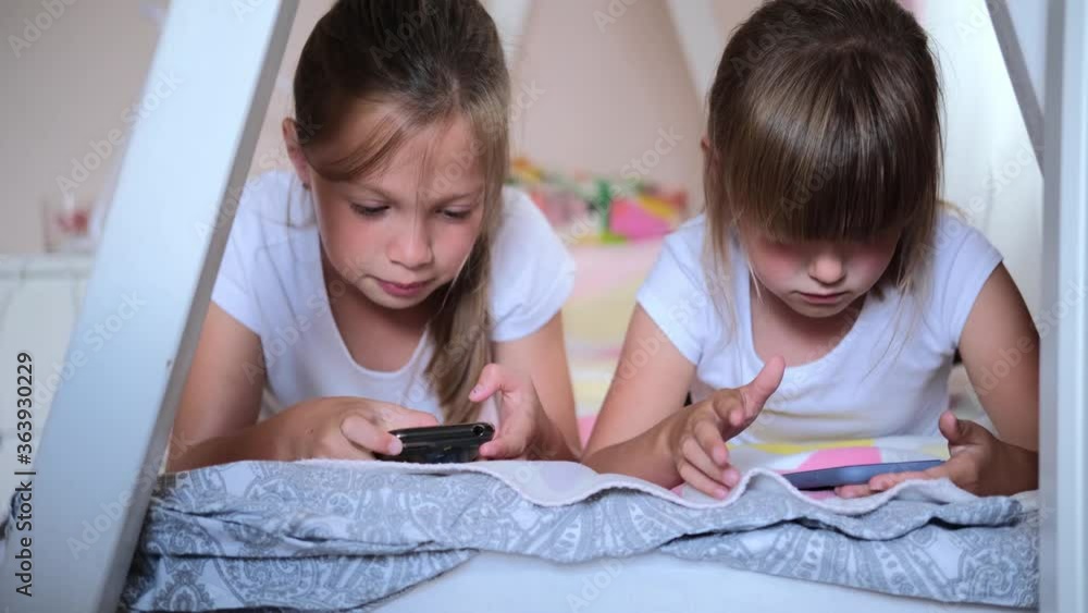 Happy little girl or child playing at home, relax, use a smartphone, sit on the couch daughter, look at the tablet screen, watch cartoons. Happy little girl or child playing at home, relax, use a smartphone, sit on the couch daughter, look at the tablet screen, watch cartoons.