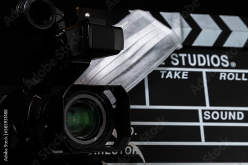 lente de câmera de filmagem em close up, no fundo claquete com máscara de proteção.	