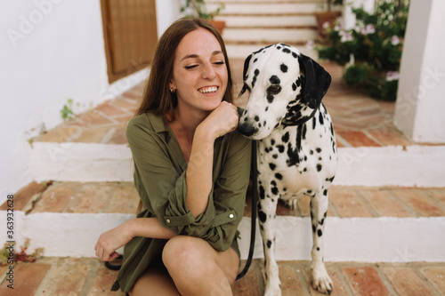 woman laughing sitting on a step and playing with her Dalmatian dog