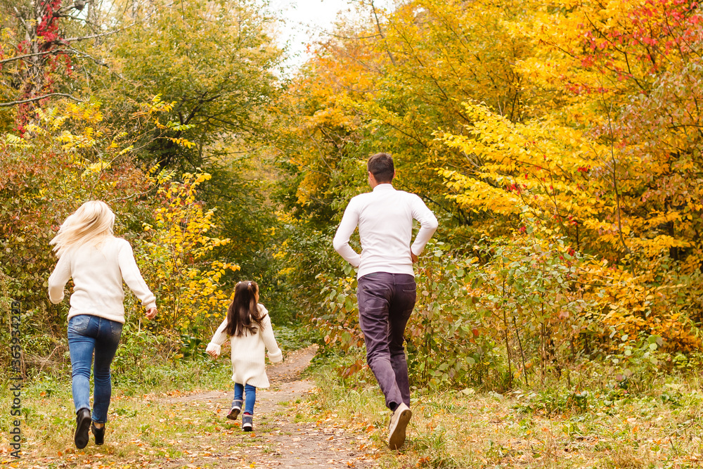 Fototapeta premium Picture of lovely family in autumn park, young parents with nice adorable daughter playing outdoors, have fun on backyard in fall, happy family enjoy autumnal nature