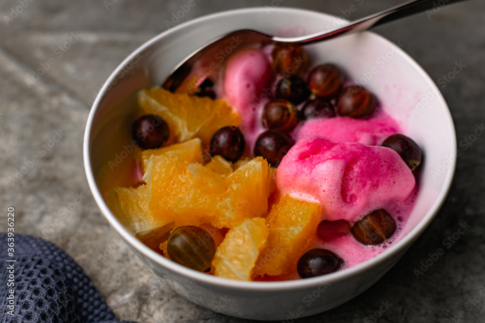 Summer refreshing dessert with fruit and berries. Pink ice cream in a bowl with orange pulp and gooseberry berries. Summer refreshing dessert with fruit and berries. Pink ice cream in a bowl with orange pulp and gooseberry berries.