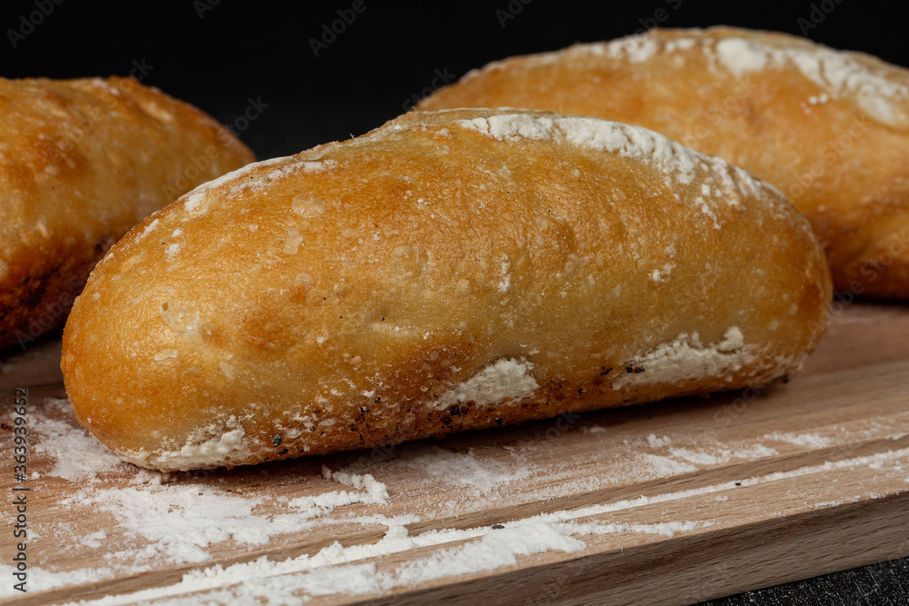 fresh white bread on a cutting board with flour on a black wooden table