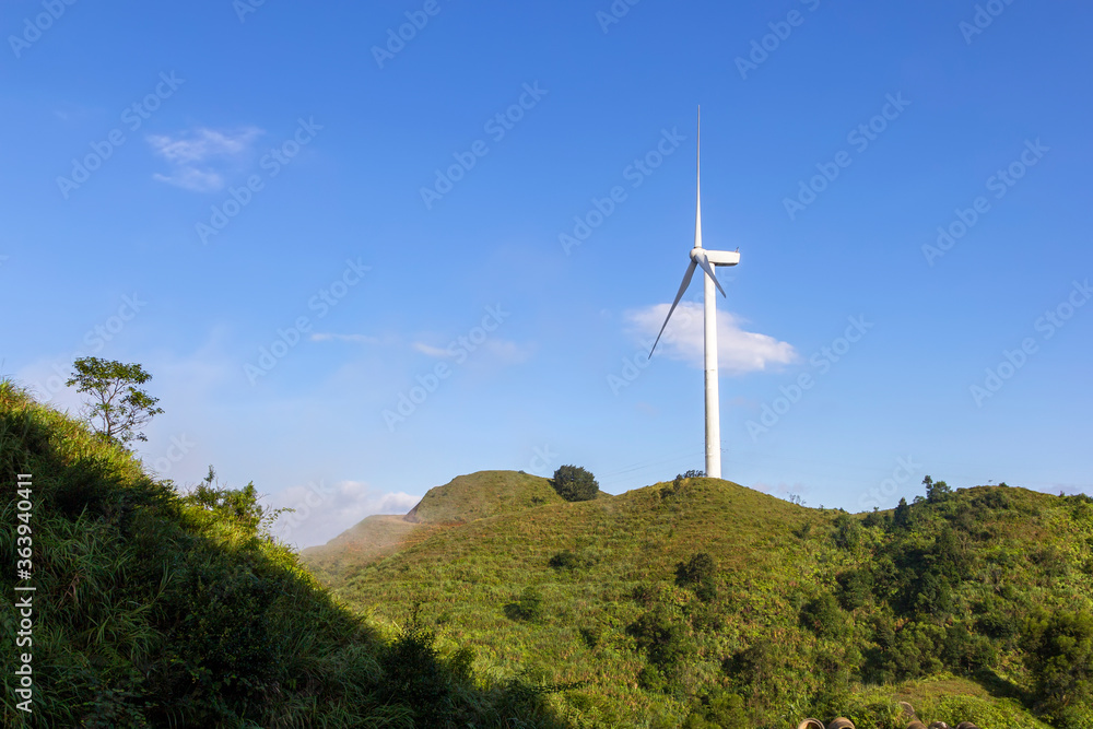 Under the blue sky and white clouds a wind turbine is built on a green mountain Under the blue sky and white clouds a wind turbine is built on a green mountain