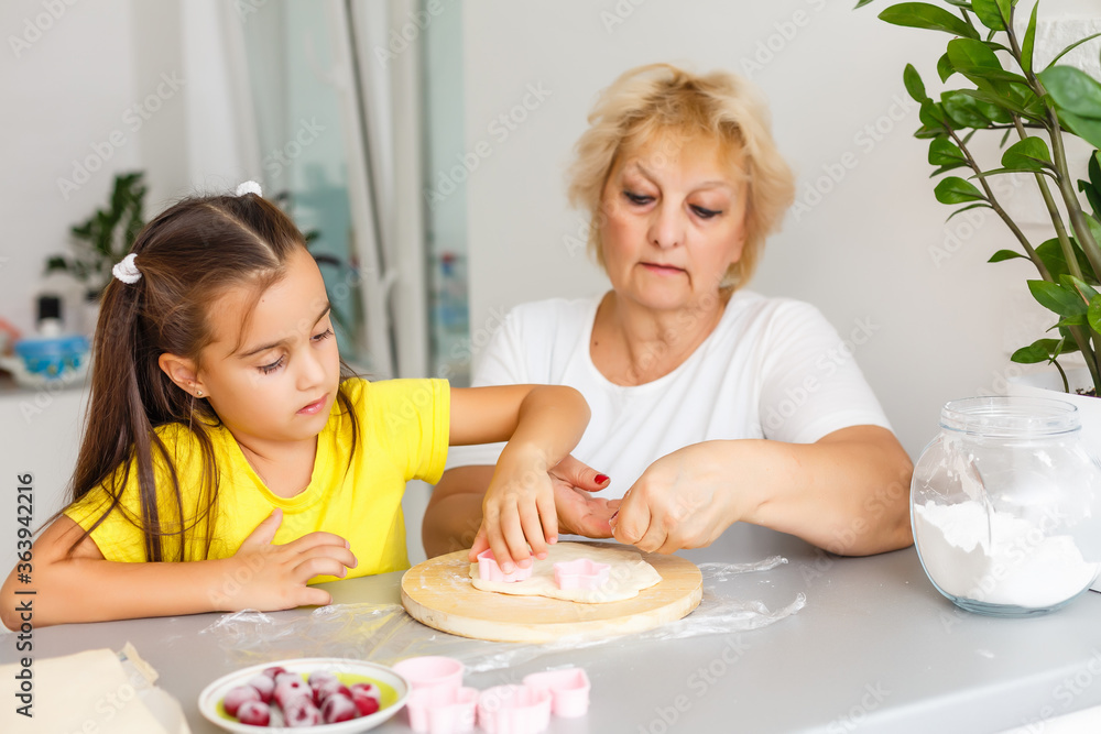 Cute little girl and her grandmother make cookies on kitchen.