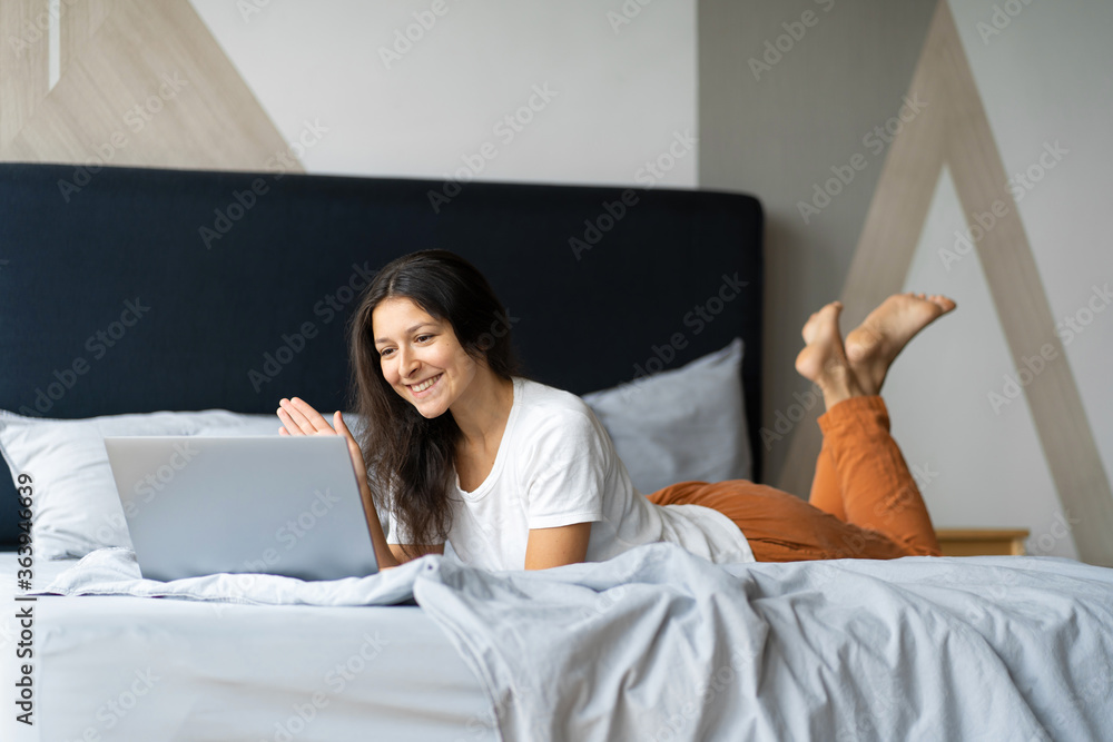 Beautiful young brunette girl with a laptop lying on the bed. Stylish modern interior. A cozy workplace. Shopping on the Internet. Beautiful young brunette girl with a laptop lying on the bed. Stylish modern interior. A cozy workplace. Shopping on the Internet.