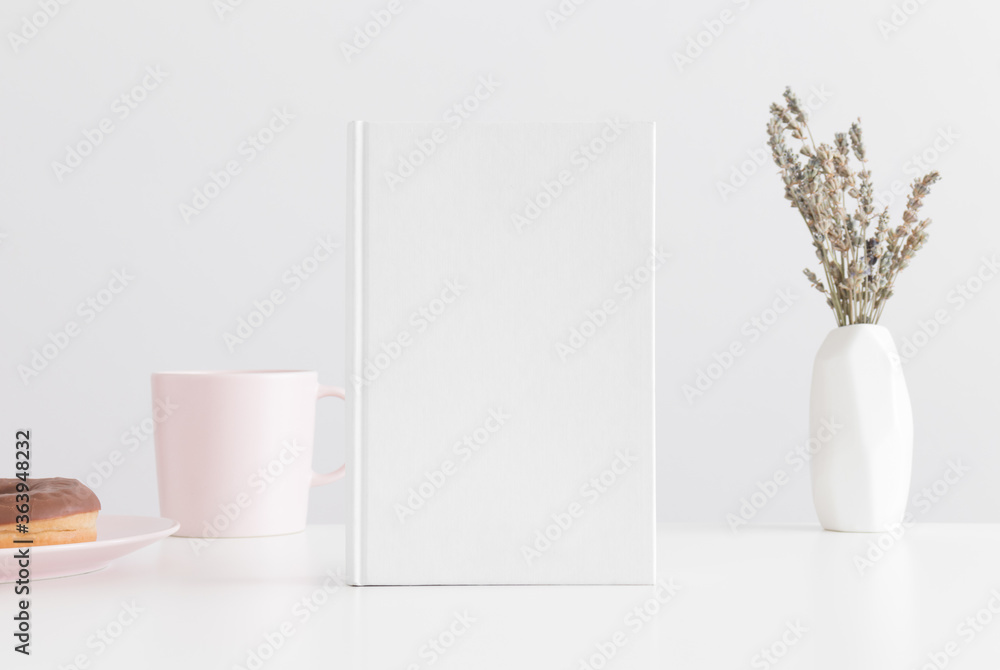 White book mockup with a mug, donut and lavanda in a vase on a white table. White book mockup with a mug, donut and lavanda in a vase on a white table.