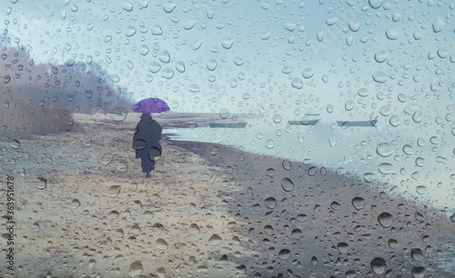 Woman walking on sandy beach of the Baltic Sea during autumnal rain, all land...