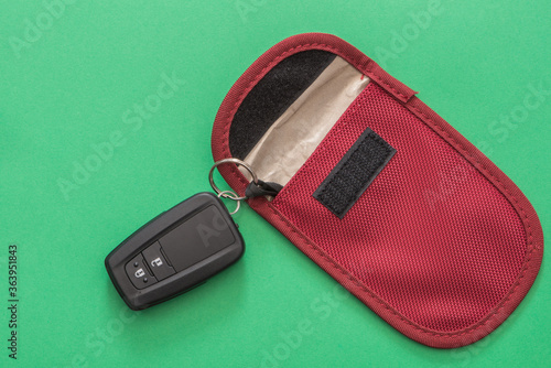 A car key fob for Keyless entry on a modern motor vehicle, with a signal blocking pouch for theft prevention. Green background, close up view.