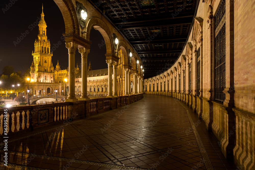 Spanish Square - A wide-angle night view of illuminated the north wing of the semi-circular brick building, as seen from ground-level portico, at Spanish Square - Plaza de España, Seville. Andalusia, 