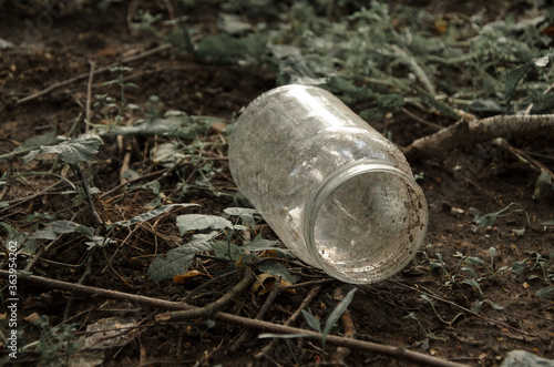 Empty dirty glass jar on the ground among grass and branches. Concept: environmental pollution, difficult to recycle waste, environmental problem. Selective focus, vintage toning.