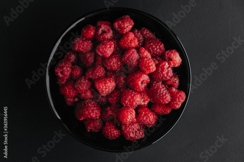 Fresh raspberries in black bowl on a dark table. closeup. Top view. Place for copy space. 