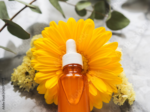 Skin care Vitamin C serum in orange bottle with dropper over beautiful yellow flowers on marble table. Natural anti aging beauty product  closeup