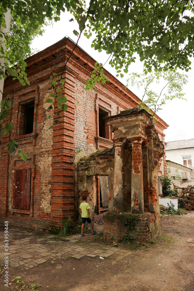 Young curious tourist boy explore the old abandoned ruined red brick house in the old russian outback town Ostashkov Young curious tourist boy explore the old abandoned ruined red brick house in the old russian outback town Ostashkov
