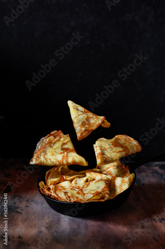 Crepe pancakes in black pan, dark background. Levitation food photography. Traditional French crepe Suzette with fresh orange sauce. Copy space, selective focus. Conceptual food image. photo