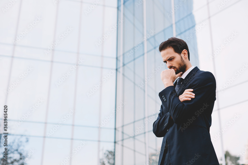 Half length portrait of confident young business man standing with arm crossed and hand against his mouth Half length portrait of confident young business man standing with arm crossed and hand against his mouth