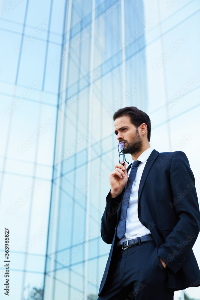 Man millionaire dressed in luxury suit having rest before meeting with potential buyers shares of his company, confident male financier having work break while standing outdoors against skyscraper Man millionaire dressed in luxury suit having rest before meeting with potential buyers shares of his company, confident male financier having work break while standing outdoors against skyscraper