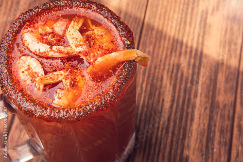 Michelada beer with tomato juice and shrimp. Clamato with beer on wooden table. Mexican drink. Vertical shot. Mexican food. photo