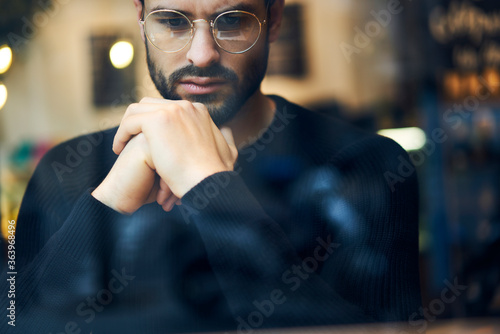 Close up of pondering trader in stylish eyeglasses thinking on solving problem.Cropped image of hipster guy in optical spectacles dressed in casual outfit analyzing information sitting indoors